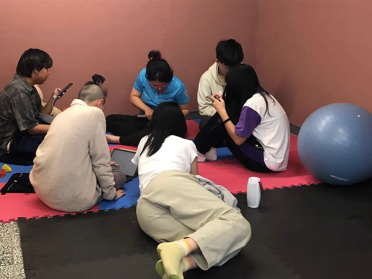 一群人在軟墊上各自做事，有人聊天、有人滑手機、有人躺著
